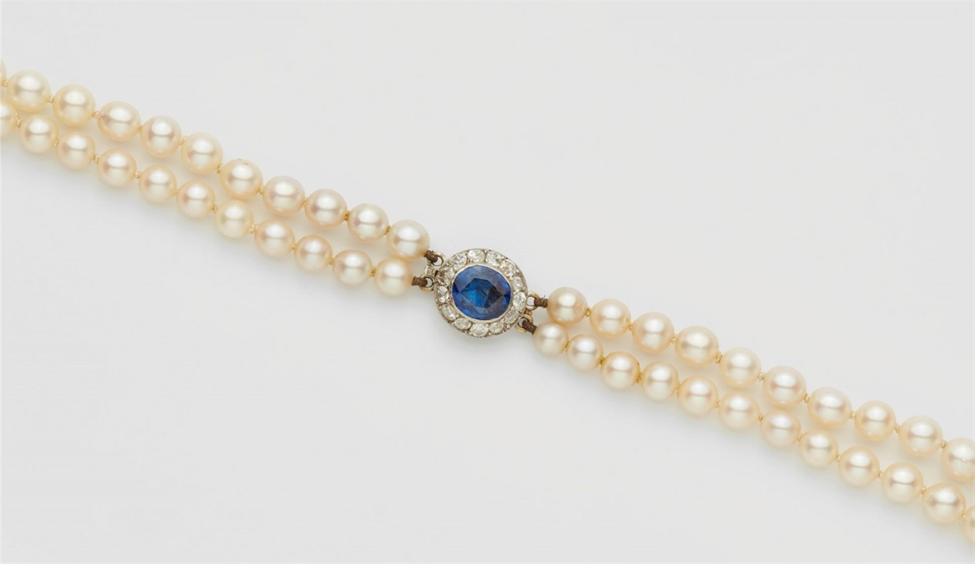 A pearl necklace with a diamond and sapphire claspA two-stranded necklace of 75/79 graduated