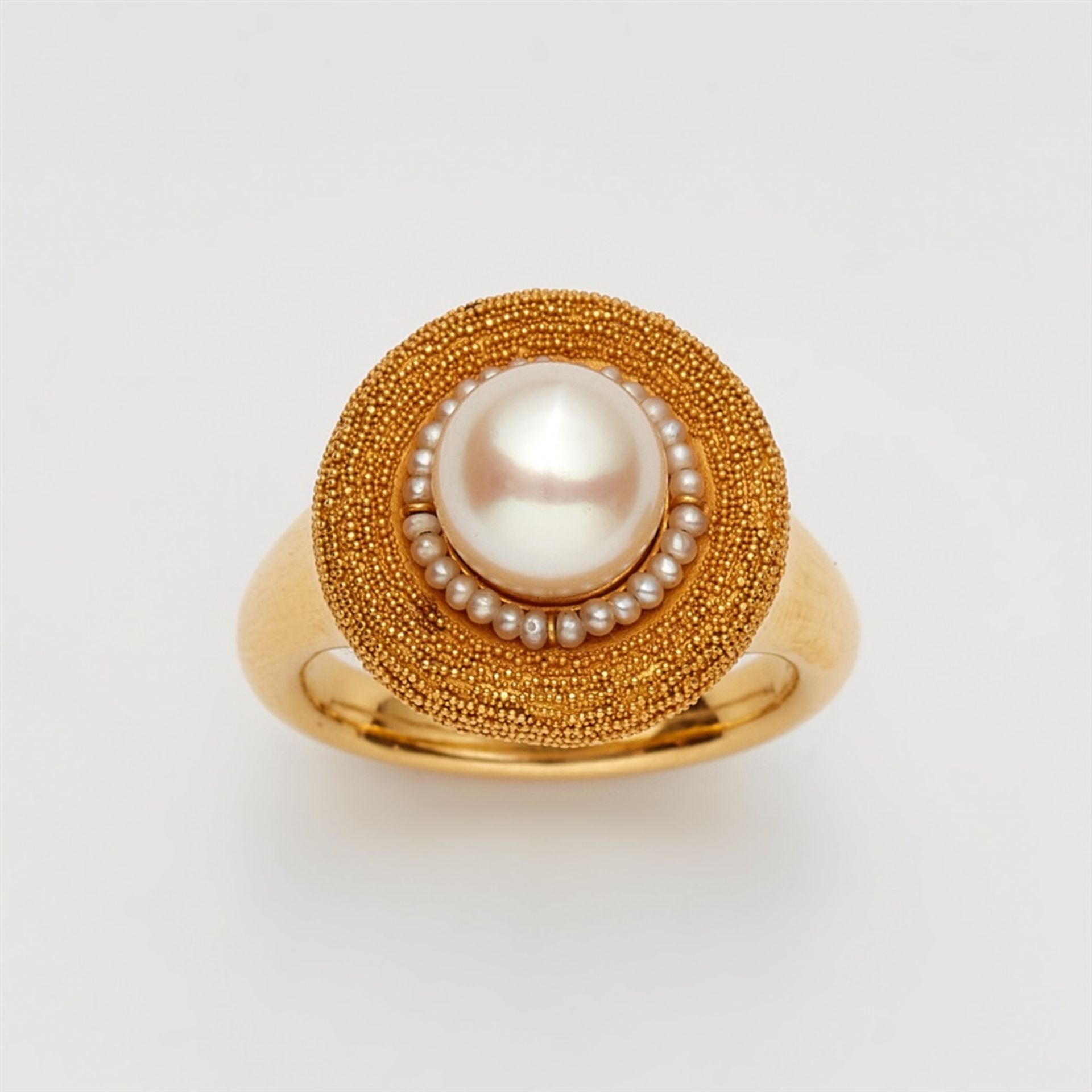 An 18k gold and pearl ringThe round bezel with fine granulation and set with a cultured pearl