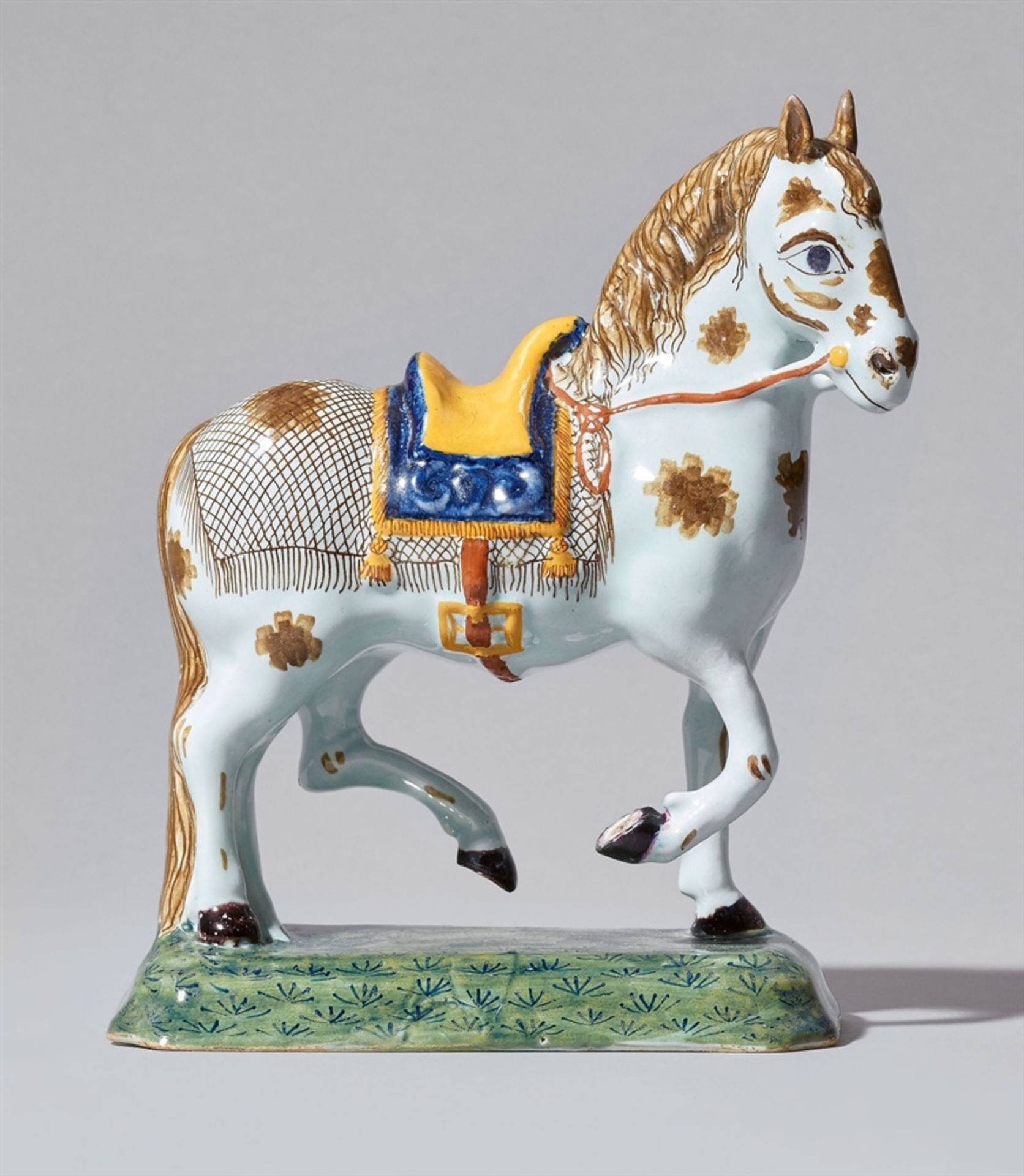 A Delftware faience model of a striding horseA horse with saddle, blanket and bridle on an oblong