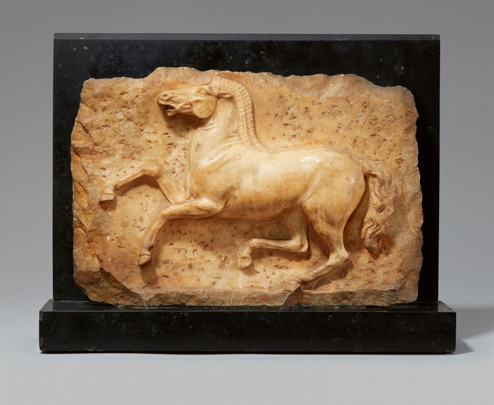 A marble relief of a jumping horsePale yellow marble on a black marble base. H c. 27.5, W c. 40