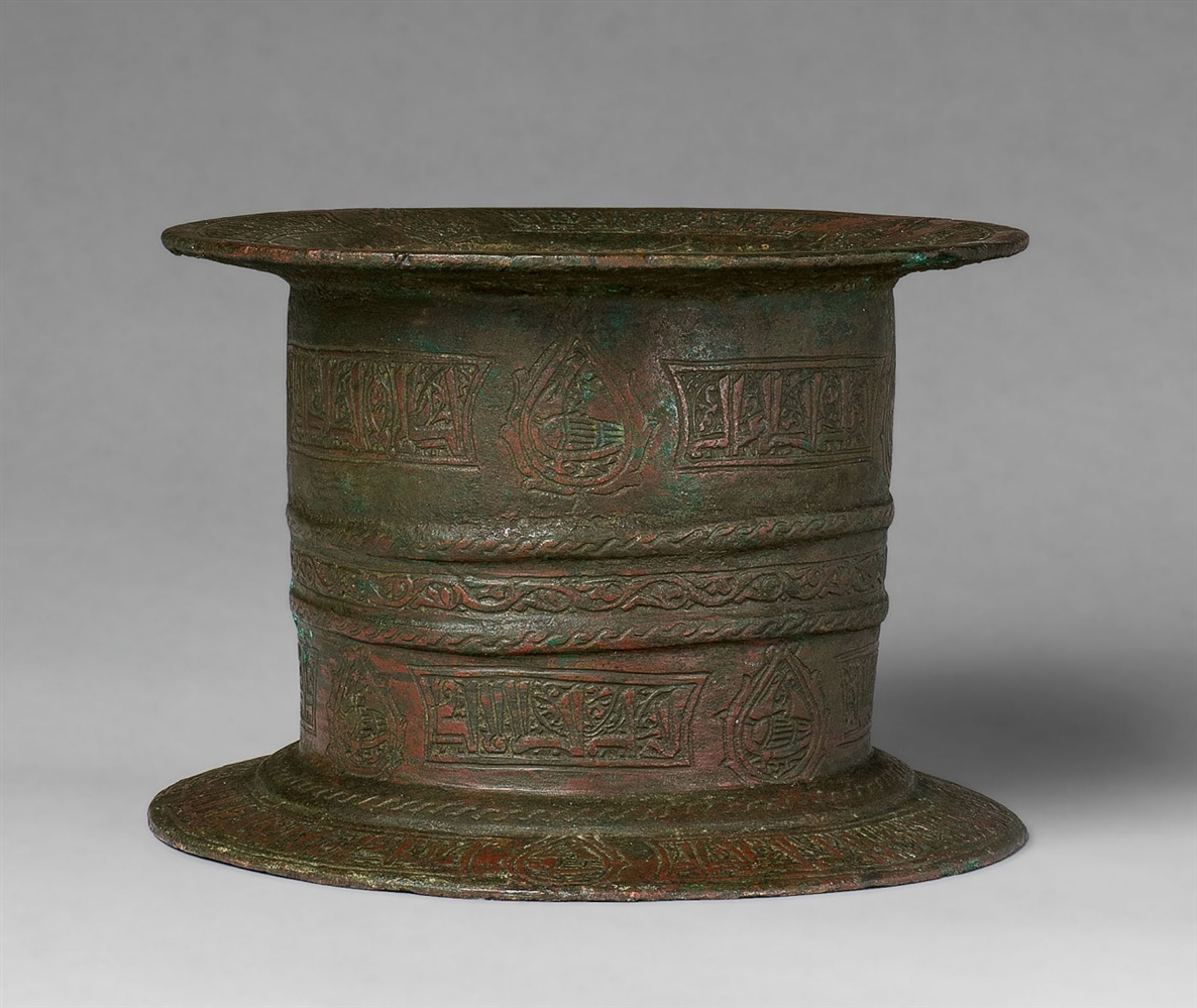 An Islamic mortarCast and chased bronze with remnants of red pigment. Cylindrical form with broad