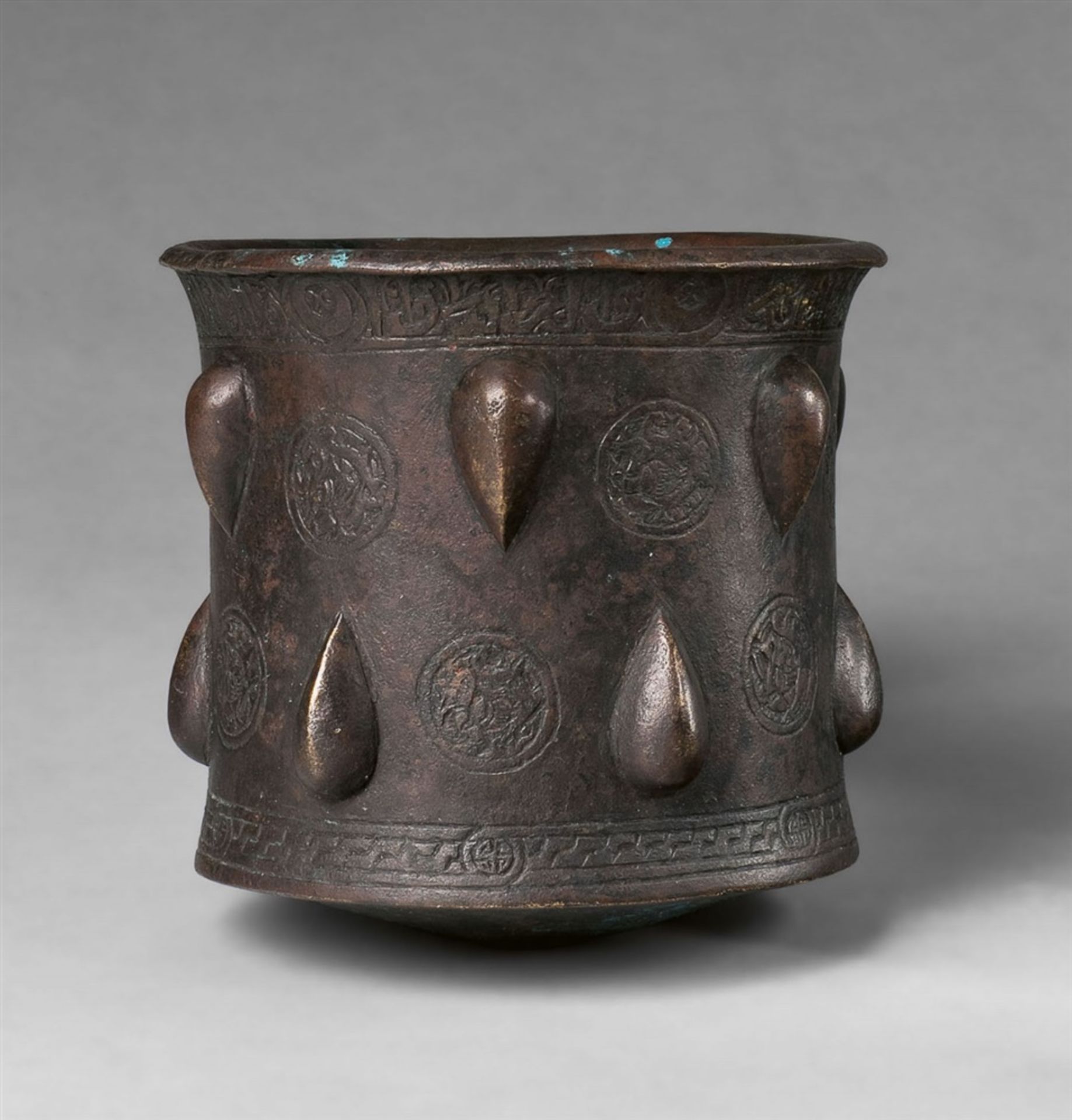 An Islamic mortarCast and chased bronze, possible sintered early polychromy. Cylindrical form with