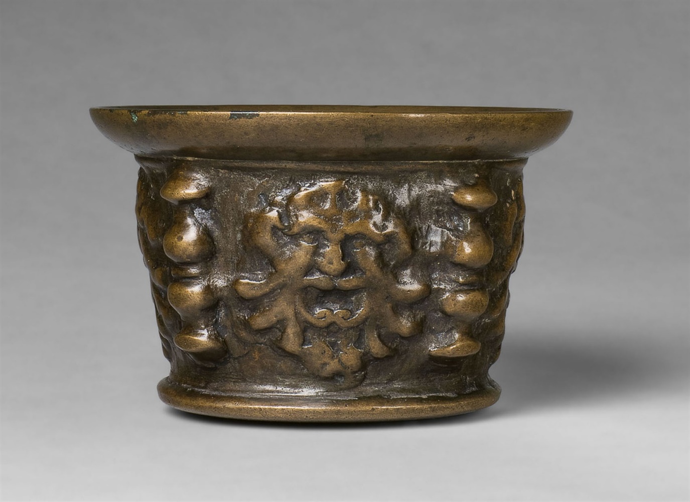 A mortar with mascaron decorThick cast bronze with natural patina. Of squat, tapering form with a