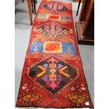 Eastern wool hand-knotted runner with three lozenge medallions upon a dark red ground, width 30in