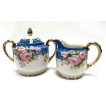 A Japanese Nippon porcelain lidded sugar bowl and milk jug, painted with roses on a blue ground.