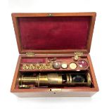 An early 20th century brass lacquered microscope with various accessories within a fitted mahogany