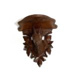 A Black Forest small wall bracket, carved with the head of a goat amongst pine leaves and with glass