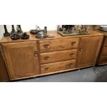 Ercol pale elm sideboard with three drawers flanked by two cupboard doors, length 156cm.