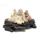 A Chinese soapstone Buddha group upon carved wood stand, width of group 7cm.