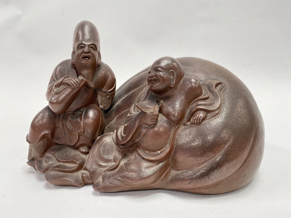 A Chinese stoneware Yixing group modelled as a reclining jovial Buddha against a pillow with