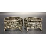 Pair of continental white metal salts with clear glass liners with pierced foliate scroll