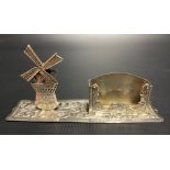 Continental white metal match box holder with articulated windmill and on a foliate embossed base,