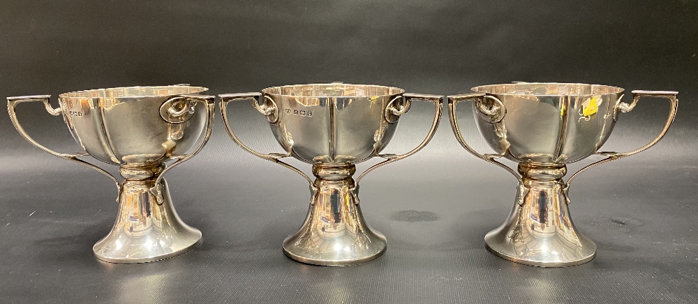 A good set of three Edwardian Art Nouveau three handled pedestal cups by William Aitken, the lobed