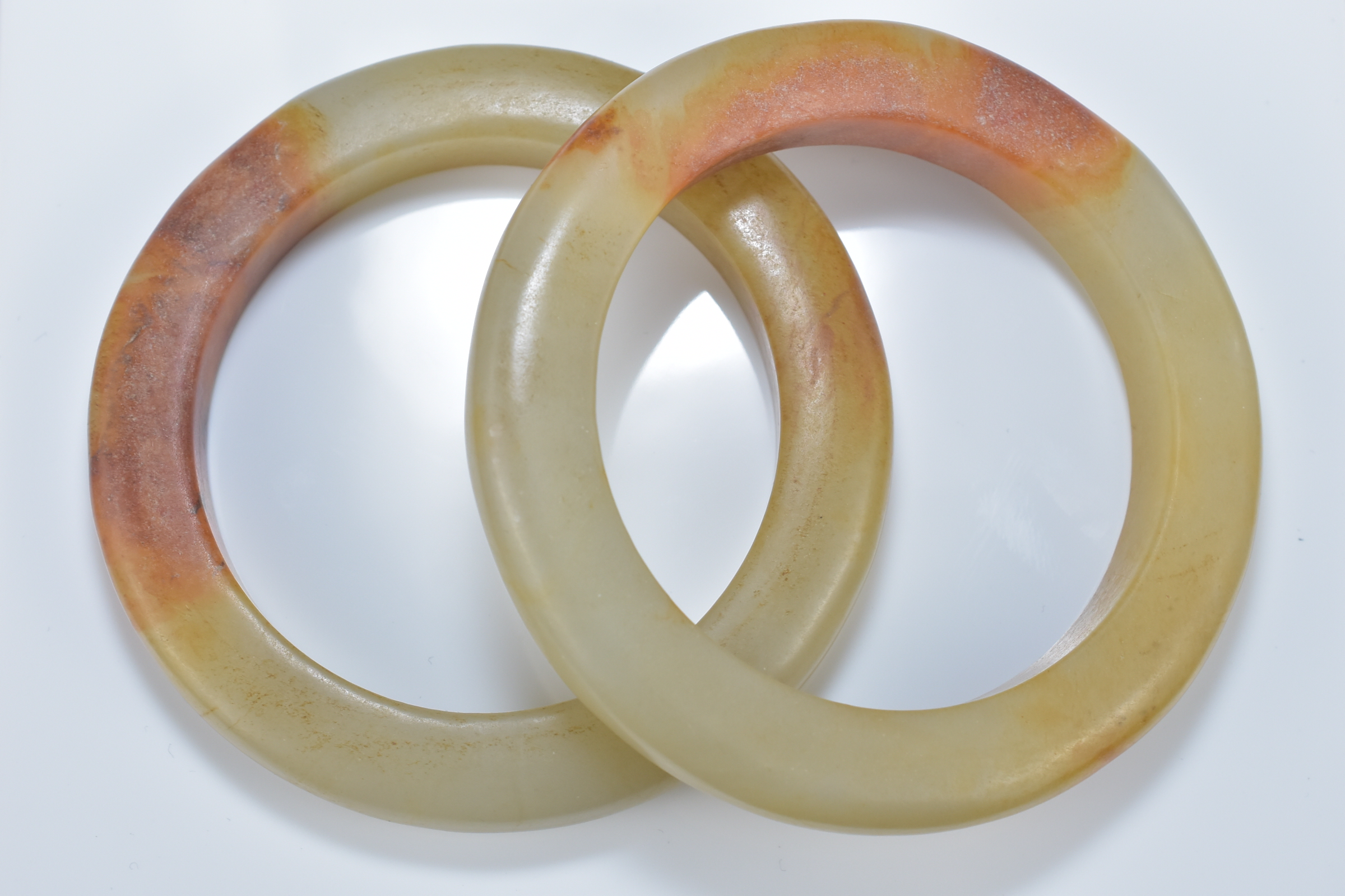 Two Chinese celadon and brown jade bangles. 8.5cm diameter. Inner diameter 6cm.