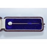 A natural baroque pearl on gold pin in original fitted box. 6.5mm length