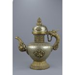 A large Tibetan brass ewer and cover with linked chain heavily decorated with repousse work and pane