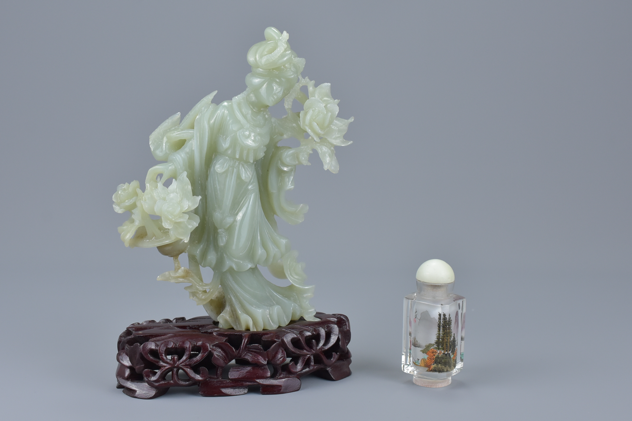A Chinese jade figure of a Goddess holding flowers on a carved wooden stand together with a small re