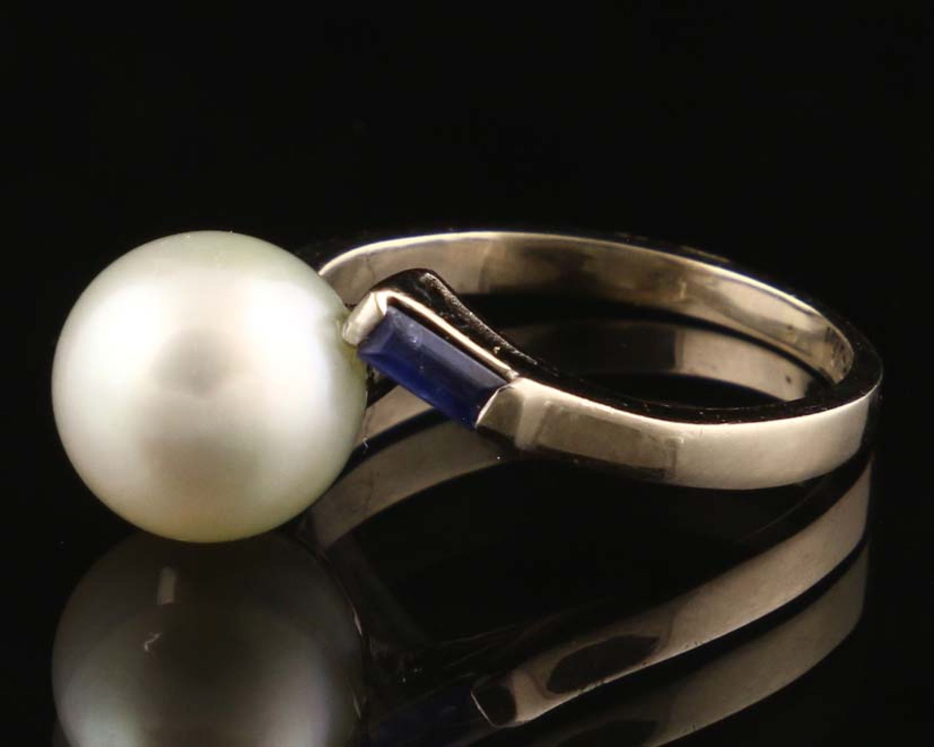 18k white gold ring centered by a cultured grey pearl, flanked by two baguette cut synthetic