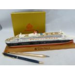 Cunard - a metal model of the Queen Mary 2, on wooden plinth; a ball point pen; and a boxed set of
