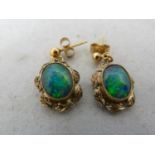 A pair of opal drop earrings, the oval stones set in yellow meal leaf decorated frams on stud drops,