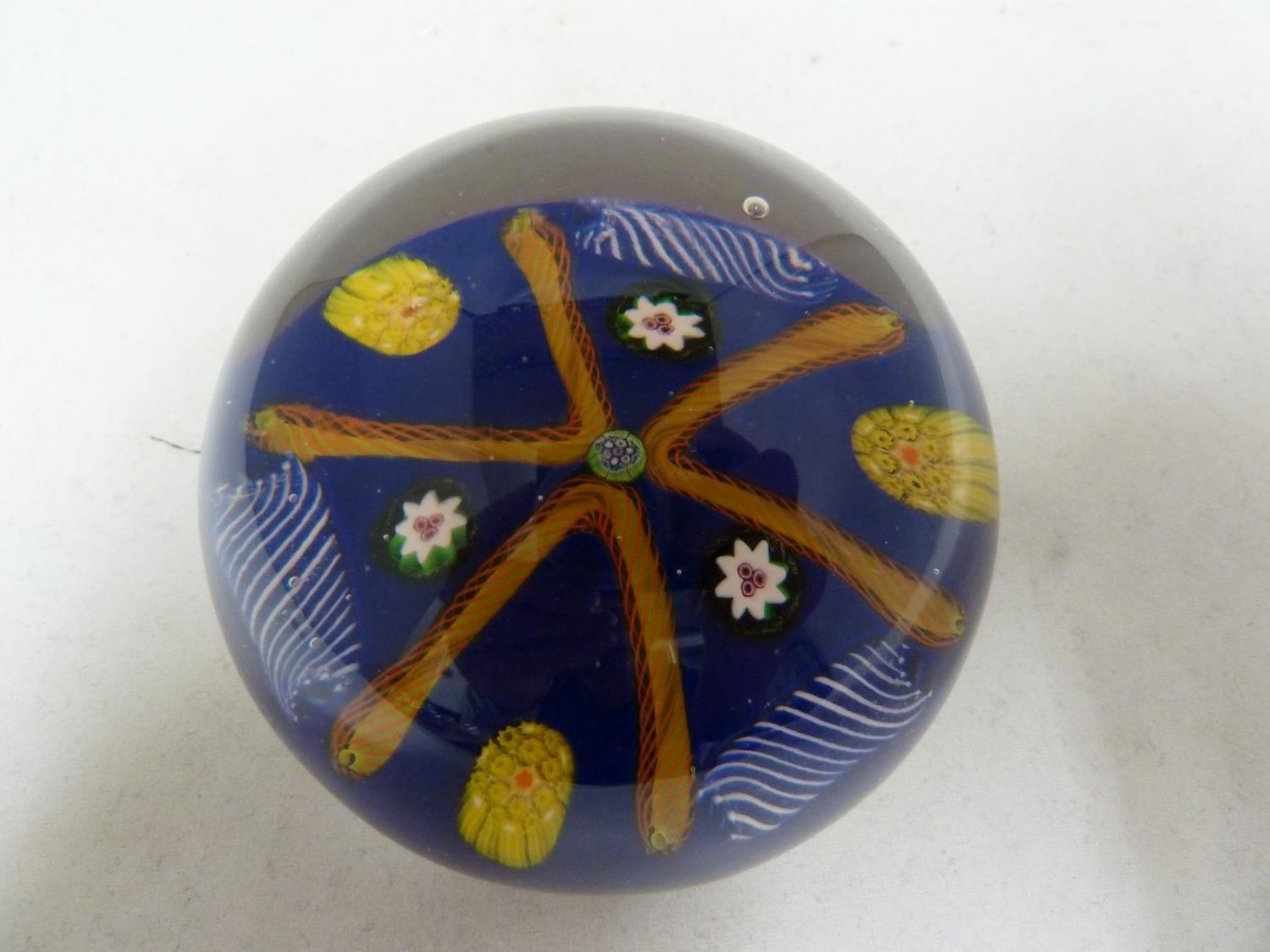 Paul Ysart - a glass paperweight, blue ground, decorated with a star of orange twist canes, 7.5cm