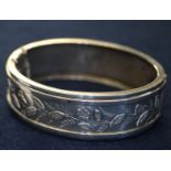 Victorian silver bangle, decorated in relief with foliage, hinged with safety chain. (B.P. 24% incl.