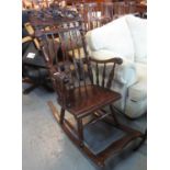 Reproduction hardwood slat and spindle back rocking armchair with carved foliate cresting. (B.P. 21%