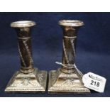 Pair of silver repousse dwarf candlesticks decorated with trailing swags on gadroon square bases.