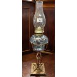 Brass single burner oil lamp with wrythen coloured glass reservoir on a stylised brass pedestal on