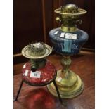 Brass double burner oil lamp on coloured glass reservoir with wrought metal three legged base,