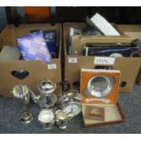 Two boxes of assorted metalware and other items to include; placemats, teaware, goblets, alarm clock