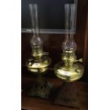 Two similar brass oil lamps with cast iron pierced bases and clear chimneys. (2) (B.P. 21% + VAT)