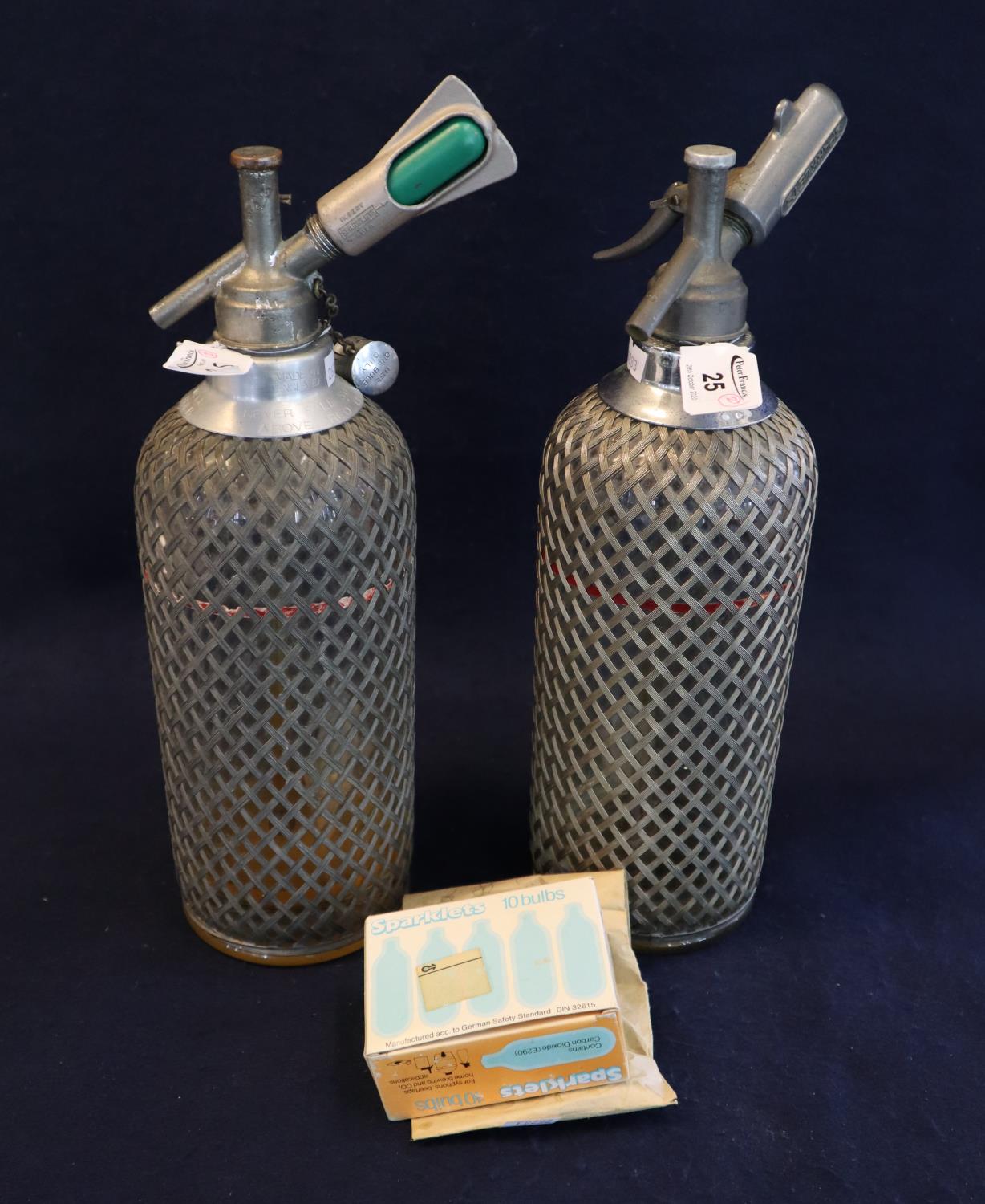 Two similar vintage soda syphons with metal wicker finish mounts and a box of Sparklets bulbs. (B.P.