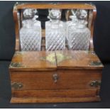 EDWARDIAN OAK THREE BOTTLE TANTALUS having originally plated mounts to angles and corners,