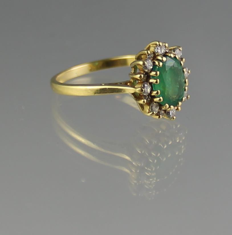 18CT GOLD EMERALD AND DIAMOND CLUSTER RING. The oval deep green claw set emerald (8 x 6mm approx)