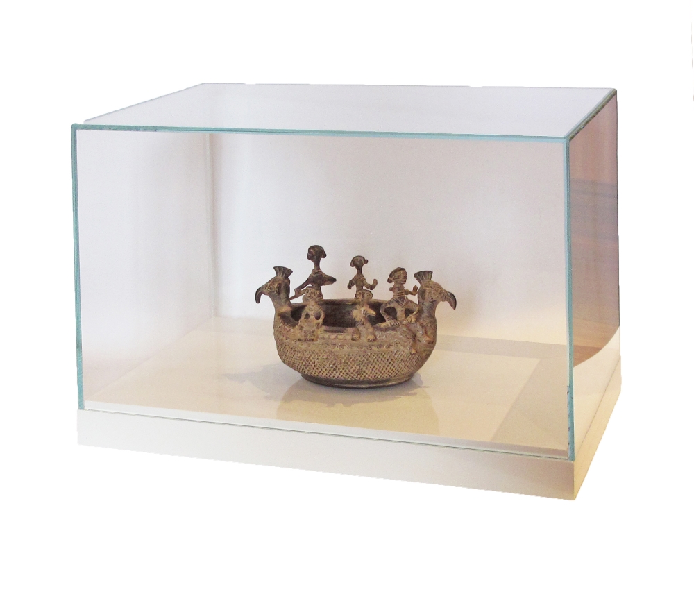 A bronze vessel / boat, in a glass display box on a white plinth. The boat 22X14cm, the glass box
