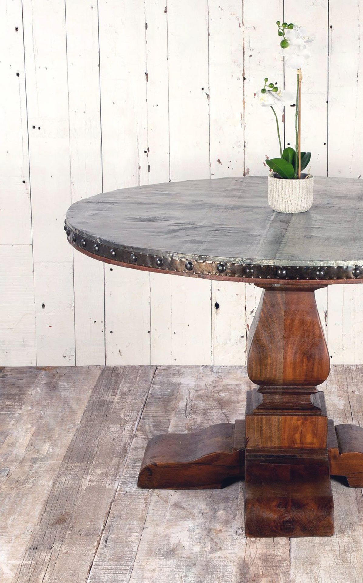 A round rustic table top with an aged metal top is supported by a wooden base forming this