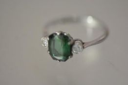 A three stone ring, the central stone possibly a green sapphire, between a pair of round brilliant-