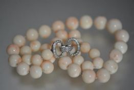 A diamond-set single strand pink coral bead necklace, the graduated strand of (undyed) pale speckled