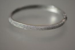 A diamond bangle in 18ct white gold, half pave set with diamonds, hinged, maker's mark "Damas".