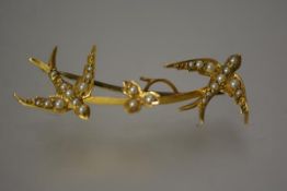 A Victorian gold and seed pearl bar brooch, modelled with a pair of swallows, flanking a leaf on a