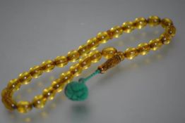 A single strand of uniform golden amber beads, oval, with a baluster shaped oval pendant