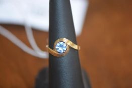 A lady's dress ring set with a single blue stone on yellow metal band marked 750