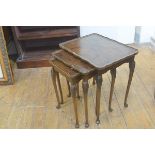 A figured walnut nest of three coffee tables, the tops with scalloped borders, raised on carved moul