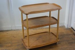 An Ercol light elm three tier trolley with part moulded edges, raised on turned supports, with