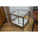 A 1970s brass two tier lamp table with inset glass panel and mirror panel to base, on square