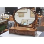 An Edwardian mahogany swing mirror, the oval mirror raised on scroll end supports, with serpentine