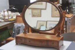 An Edwardian mahogany swing mirror, the oval mirror raised on scroll end supports, with serpentine