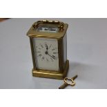 A French four glass brass clock with enamelled dial and roman and arabic numerals, complete with key