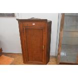 A George III oak hanging corner cupboard, with single panelled door (section of cornice missing).